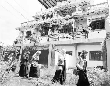  ??  ?? Residents who returned from evacuation centers walk past a bullet-ridden house believed to have been rented by pro-Islamic State militant group leaders Isnilon Hapilon and Omar Maute before their attack on the region, in Basak, Malutlut district in...