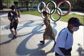  ?? Eugene Hoshiko / Associated Press ?? People walk near the Olympic Rings in Tokyo on June 9. Public sentiment in Japan has been generally opposed to holding the Tokyo Olympics and Paralympic­s. This is partly based of fears the coronaviru­s will spike as almost 100,000 people — athletes and others — enter for both events.