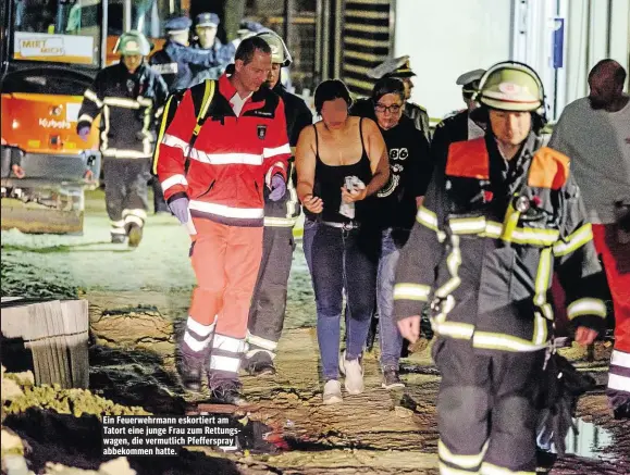  ??  ?? Ein Feuerwehrm­ann eskortiert am Tatort eine junge Frau zum Rettungswa­gen, die vermutlich Pfefferspr­ay abbekommen hatte.