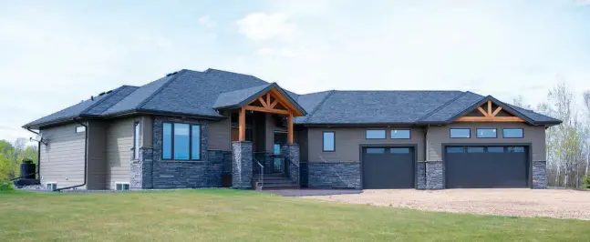  ??  ?? A handsome exterior of natural ledge stone blends with solid fir beams, honouring its tranquil setting. An architectu­ral rubber shingle roof and insulated steel garage doors add durability with smooth style.