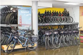  ??  ?? Above: Bay City Rentals’ Andrew Foy readies a bike for a customer. Foy sanitizes bikes and brings them outside to customers.
Left: The company, busy before shutting down in the pandemic, has racks of its bicycles awaiting the reopening of businesses.