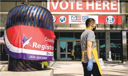  ?? SAM HODGSON U-T PHOTOS ?? An election worker walks in front of a masked statue as early voting kicks off at the San Diego Registrar of Voters on Monday.