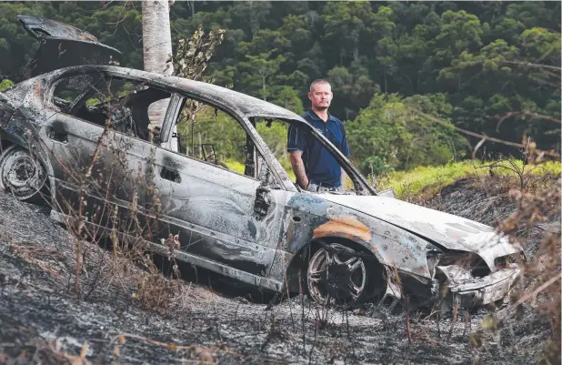  ?? Picture: BRENDAN RADKE ?? EYESORE: Bentley Park resident Brett Davenport looks over a burnt-out car dumped off Macaranga Rd earlier this week.