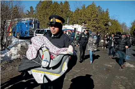  ?? PHOTO: REUTERS ?? A Royal Canadian Mounted Police officer carries a child in a car seat as the mother is escorted to a waiting vehicle after crossing the border from the United States into Hemmingfor­d, Quebec yesterday. A family of four crossed as the RCMP was...