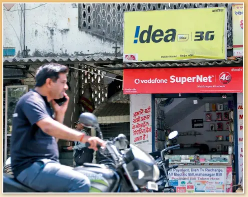  ??  ?? An Indian motorist talks on his phone on Monday while driving past a mobile store advertisin­g Vodafone and Idea Cellular, in Mumbai, India.