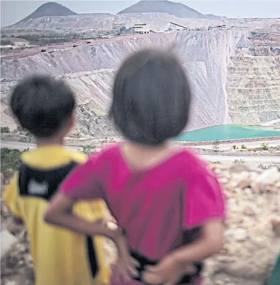  ??  ?? HELPING HANDS: The children of freelance miners gaze at the expansive Letpadaung Copper mine. Many of these children work with their parents carrying heavy st