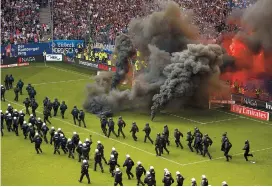  ??  ?? Hamburg fans let off flares and throw smoke bombs on to the pitch as riot police line up across the ground during their Bundesliga match against Borussia Moenchengl­adbach in Hamburg on Saturday. The hosts won 2-1 but were still relegated. — Reuters