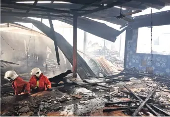  ??  ?? Firemen carry out checks at the gutted Rumah Dingun Megong in the aftermath of the blaze.