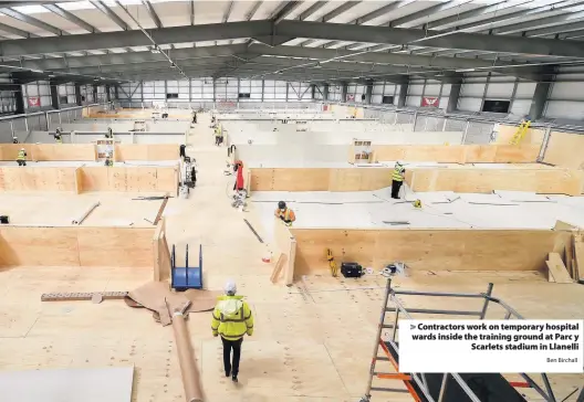  ?? Ben Birchall ?? > Contractor­s work on temporary hospital wards inside the training ground at Parc y Scarlets stadium in Llanelli
