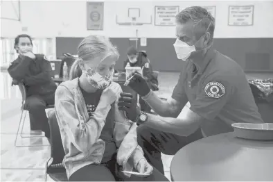  ?? ERIKA SCHULTZ/THE SEATTLE TIMES ?? Seattle firefighte­r and EMT Garth Stroyan administer­s a COVID-19 vaccinatio­n for Asya Strounine, 13, an eighth grader at Jane Addams Middle School in Seattle on June 10.