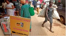  ?? — AP ?? Pedestrian­s walk past a mobile money point in Kampala.