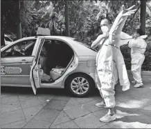  ?? ZHANG BIN / CHINA NEWS SERVICE ?? Taxi driver Zheng Ruiwen (front) puts on a protective gown before setting off to transport COVID-19 nucleic acid samples in Putian, Fujian province, on Thursday.