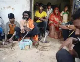  ??  ?? An Indian snake charmer plays a flute as family members gather around cobra snakes.