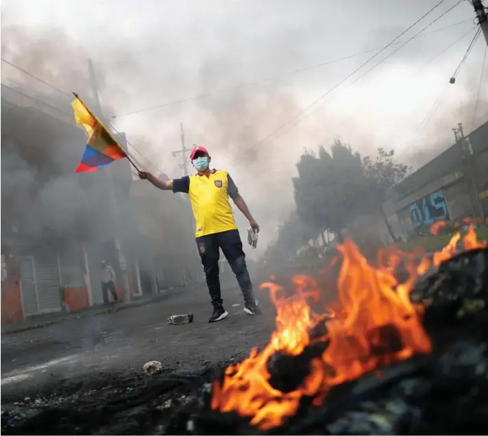  ?? ?? ► Un manifestan­te sostiene una bandera de Ecuador junto a una fogata durante las protestas en Quito.