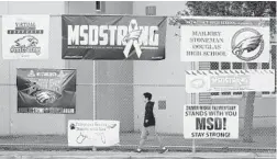  ?? WILFREDO LEE/AP ?? A student walks past signs outside Marjory Stoneman Douglas High School during the one-year anniversar­y of the school shooting.