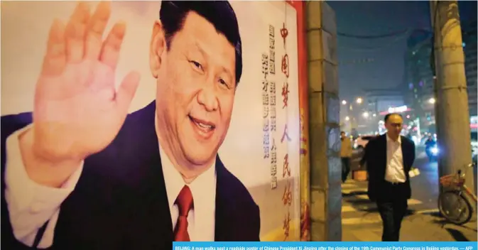  ?? — AFP ?? BEIJING: A man walks past a roadside poster of Chinese President Xi Jinping after the closing of the 19th Communist Party Congress in Beijing yesterday.