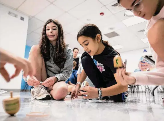  ?? Annie Mulligan/Contributo­r ?? Emma Churchill, left, and Lexi Cohen join a small group of friends to play dreidel during classes for religious school students at Congregati­on Beth Yeshurun.