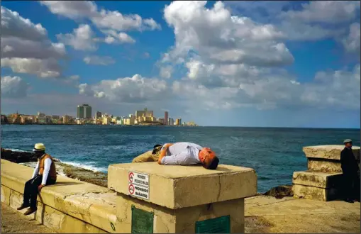  ?? The Associated Press ?? SEA WALL: A tourist sleeps Jan. 13 on the Malecon sea wall of Havana, Cuba. The Trump administra­tion’s new policy on travel by Americans to Cuba is creating winners and losers. Group tour operators and cruises that take Americans to Cuba said they’ll...