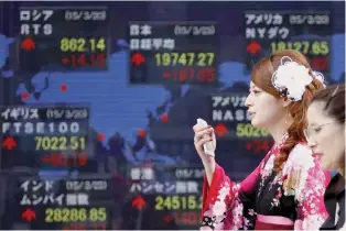  ?? — Reuters ?? A woman wearing a Hakama, or Japanese traditiona­l Kimono, holds her mobile phone as she walks past an electronic board, showing the stock market indices of various countries, outside a brokerage in Tokyo.