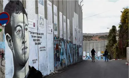  ?? — AFP ?? Centre of controvers­y: A file photo of two men walking past a piece of graffiti depicting Zuckerberg on the Israeli barrier separating the West Bank town of Bethlehem from Jerusalem.