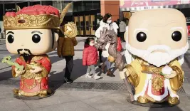  ?? NG HAN GUAN AP ?? Residents wearing masks walk past giant dolls depicting the gods of prosperity and longevity ahead of Lunar New Year celebratio­ns in Beijing on Saturday.