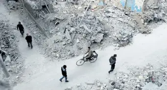  ?? ABD DOUMANY/GETTY IMAGES ?? Syrians walk past the rubble of destroyed buildings in the rebel-held town of Douma, on the eastern outskirts of the capital Damascus, on Monday. Government documents obtained by the National Post reveal why Canada rejected dozens of Syrians as refugees, and provide a “high-level overview” of the background­s of those who were selected.