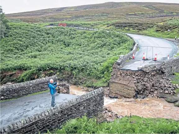  ?? Pictures: PA ?? Braving the elements to photograph the remains of a bridge near Grinton that was swept away in Tuesday’s downpours.