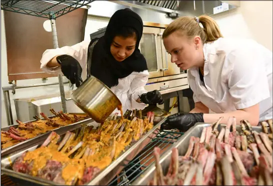  ?? ANDY CROSS — THE DENVER POST ?? Afghan refugee Shukria Mohammad pours sauce over lamb chops with help from University of Denver hospitalit­y management student Jess Bryan in the kitchen at the Joy Burns Center. The Fritz Knoebel School of Hospitalit­y Management program hosted refugees in a fiveweek food training course called the Ready for American Hospitalit­y program. The course culminated Thursday evening with DU students and staffers working together with the refugees to produce and serve a four- course meal for more than 120 guests.