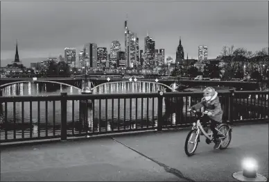  ?? MICHAEL PROBST AP PHOTO ?? A small girl wearing a face mask rides her bike over a bridge over the river Main in Frankfurt, Germany, on Thursday.