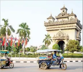  ?? AFP ?? Traditiona­l tuk tuks pass in front of the Patuxai war monument in the centre of the Lao capital Vientiane. Lao and foreign nationals and stateless people aged 12 and older who have not been fully vaccinated are required to take a Covid-19 ATK test within 48 hours of their departure for Laos.