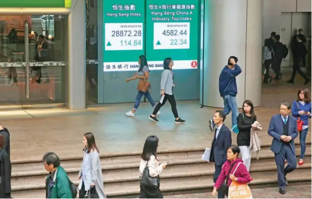  ?? Associated Press ?? ↑ People walk past a board, showing the stock index, outside a bank in Hong Kong.