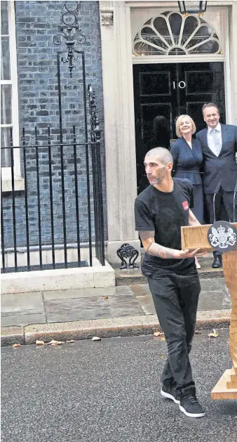  ?? ?? As workmen clear away the lectern where she made her first speech as PM, Liz Truss and husband, Hugh O’Leary, wave from the steps of 10 Downing Street on Tuesday