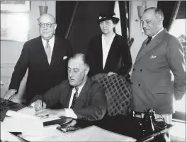  ?? THE ASSOCIATED PRESS ?? President Franklin D. Roosevelt is shown signing the Wagner Unemployme­nt Bill at the White House in Washington. Standing, from left are: Rep. Theodore A. Peyser, D-N.Y.; Labor Secretary of Labor Frances Perkins; and Sen. Robert Wagner, D-N.Y.