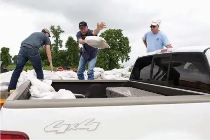  ?? Staff photo by Curt Youngblood ?? Zane Lawver, center, and David Lawver, left, load sand bags for Steve Doss at the emergency command center in Garland City, Ark. Doss is helping a friend prepare for flood waters from the Red River.