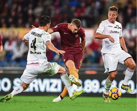  ?? Deadly: ?? AS Roma striker Edin Dzeko taking a shot at goal despite being challenged by two Palermo players in the Serie A match at the Olympic Stadium in Rome on Sunday. Roma won 4-1. — Reuters