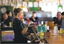  ?? DAVID J. PHILLIP AP ?? Bartender Alyssa Dooley talks with customers at Mo’s Irish Pub Tuesday in Houston. Eateries are considerin­g whether staff will still wear masks.