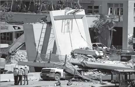  ?? WILFREDO LEE/AP PHOTO ?? Workers stand next to a section of a collapsed pedestrian bridge Friday near Florida Internatio­nal University in Miami. The new bridge, which was under constructi­on, collapsed onto a busy highway Thursday afternoon, crushing vehicles beneath massive...