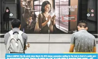  ?? —AFP ?? KUALA LUMPUR: This file photo taken March 26, 2018 shows commuters waiting for the train in-front of a public service announceme­nt that reads “sharing a lie makes you a liar” at a train station in downtown Kuala Lumpur.