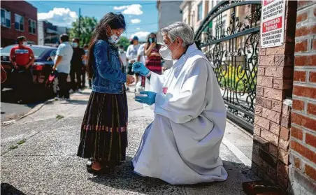  ?? Johannes Eisele / AFP via Getty Images ?? Fabian Arias, a Lutheran pastor with Saint Peter’s Church in Manhattan, gives communion to a girl as he holds a service on the street in Brooklyn on May 30. His church has lost more than 40 parishione­rs to the coronaviru­s, 90 percent of them Hispanic.
