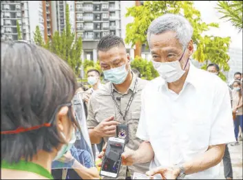  ?? The Associated Press ?? Prime Minister Lee Hsien Loong, right, verifies his identity with an official at a polling center Friday in Singapore. Lee’s party kept its sizable majority in Parliament.