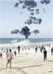  ?? AGENCE FRANCE-PRESSE ?? PALESTINIA­NS run toward food parcels attached to parachutes being air-dropped from United States aircraft on a beach in the Gaza Strip.