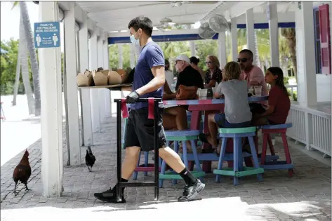  ?? LYNNE SLADKY — THE ASSOCIATED PRESS ?? In this June 1, 2020file photo, Charles Perez wears a protective face mask and gloves as he waits on tables at the Morada Bay Beach Cafe in Islamorada, in the Florida Keys, during the new coronaviru­s pandemic. Repealing statewide mask mandates and criticizin­g the Biden administra­tion’s unemployme­nt-based formula for distributi­ng billions in federal aid has put Republican governors and their approach to handling the coronaviru­s pandemic back in the spotlight.