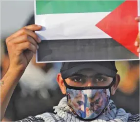  ??  ?? An Iraqi demonstrat­or wearing a face mask lifts the Palestinia­n flag during a anti-Israel protest in Baghdad, yesterday.