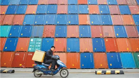  ?? Reuters-Yonhap ?? A man rides his motorcycle past shipping containers at the Port of Shanghai, Feb. 14, 2011.