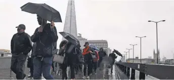  ?? JUSTIN TALLIS, AFP/ GETTY IMAGES ?? Commuters walk in the rain past a security barrier installed between the pavement and the road on London Bridge.