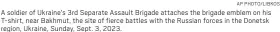  ?? AP PHOTO/ LIBKOS ?? A soldier of Ukraine’s 3rd Separate Assault Brigade attaches the brigade emblem on his T-shirt, near Bakhmut, the site of fierce battles with the Russian forces in the Donetsk region, Ukraine, Sunday, Sept. 3, 2023.