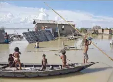  ?? —- Reuters ?? Children row a boat as they pass through damaged houses at a flood-affected village in Morigaon district of Assam on Sunday.