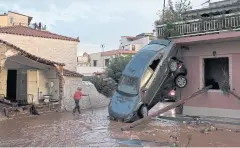  ?? AP ?? A woman walks on a flooded street next to damaged houses and cars flipped by floodwater against a wall in the municipali­ty of Madra, western Athens on Wednesday.