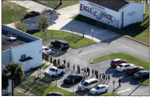  ?? AP/South Florida Sun-Sentinel/MIKE STOCKER ?? A police officer leads a group of students out of Marjory Stoneman Douglas High School after a shooting Wednesday on the campus that left more than a dozen people dead.