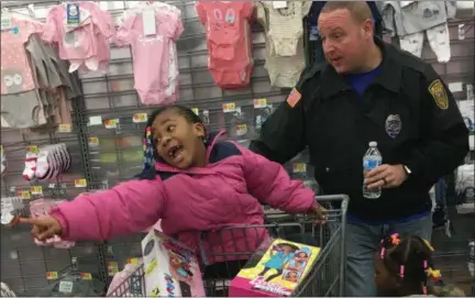  ?? RICHARD PAYERCHIN — THE MORNING JOURNAL ?? Lorain Police Officer Jacob Morris works with shoppers, DeCarri Burrell, 5, in the cart, and Avaya Goodwin, 2, during Cops and Kids holiday shopping event, sponsored by the Fraternal Order of Police-Lorain Lodge No. 3 on Dec. 15 at the Walmart Supercente­r in Lorain.